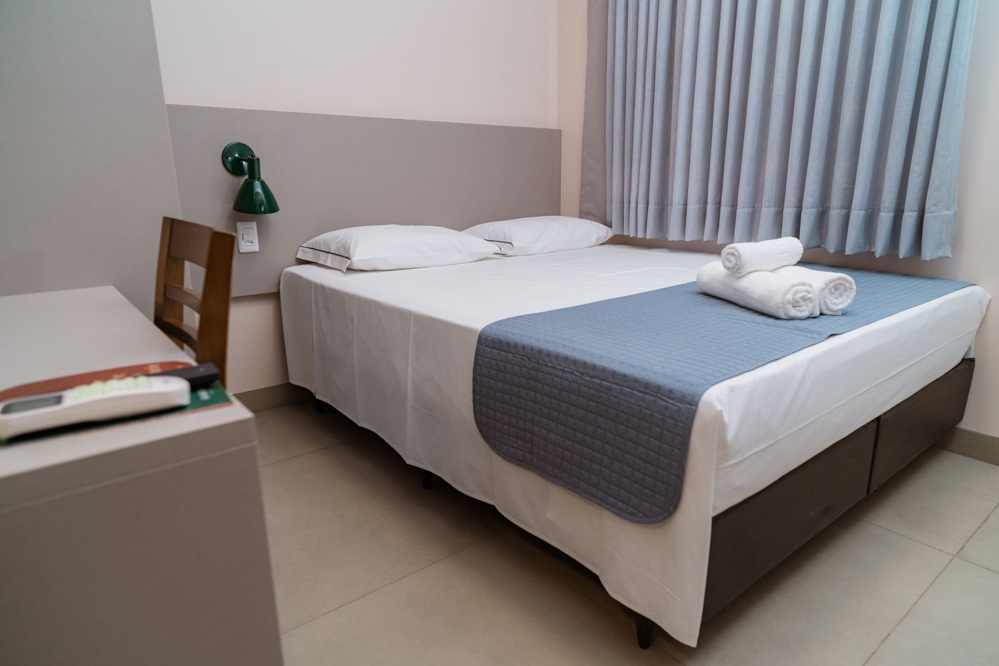 Quarto Single com cama de casal, mesa de trabalho e cortina azul
